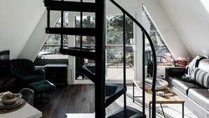 Moderni loft-tyylinen asunto, jossa on musta, spiraalimainen portaikko, viihtyisä oleskelualue ja suuret ikkunat, joista on näkymä ulos.