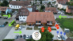Vista aérea de una zona residencial con espacios de estacionamiento numerados, un autobús amarillo y un edificio con techo rojo.