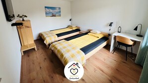 Una habitación con dos camas, un escritorio, una silla, una mesita, un televisor y un cuadro en la pared.