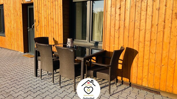 Edificio de madera con un patio que tiene sillas de mimbre y una mesa.