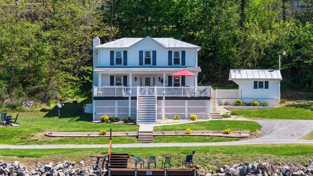 A two-story house with a porch, a dock extending into a body of water, and a small shed nearby. - The River House, Pet Friendly with a Hot Tub 15 Minutes to many attractions!! (Shenandoah)