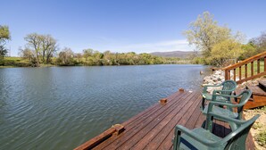 A wooden deck with chairs overlooking a calm river, surrounded by trees and a clear sky. - The River House, Pet Friendly with a Hot Tub 15 Minutes to many attractions!! (Shenandoah)