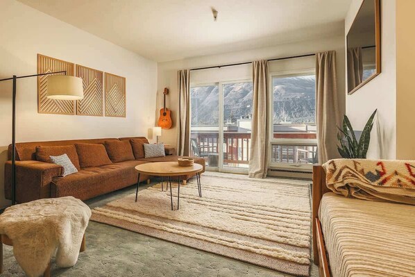 Ein gemütliches Wohnzimmer mit einer Couch, einem Couchtisch und Bergblick durch große Fenster.