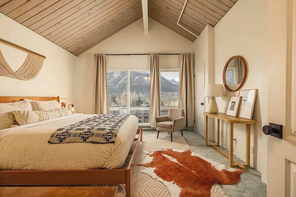 Une chambre à coucher avec un lit, une chaise, un miroir et une vue sur les montagnes, visible à travers de grandes fenêtres.