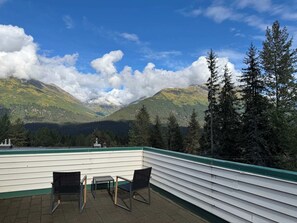 Une terrasse avec une table et deux chaises, offrant une vue sur un paysage montagneux, avec des arbres et un ciel dégagé.