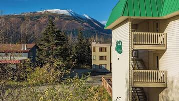 A building with a green roof and a balcony, surrounded by trees and a mountain in the background.