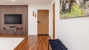 Una sala de estar moderna con un televisor de pantalla plana montado en una pared de paneles de madera, piso de madera y una puerta al fondo.