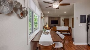 Una cocina moderna con comedor, suelo de madera, ventilador de techo y un amplio ventanal que proporciona luz natural.