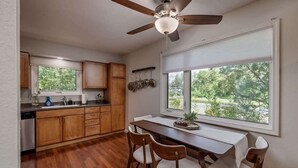 Una cocina con armarios de madera, una mesa de comedor con sillas, un ventilador de techo y una ventana con persianas.
