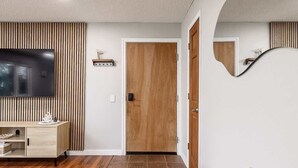 Una sala de estar moderna con pared de madera, televisor de pantalla plana, puerta de madera y sofá blanco.