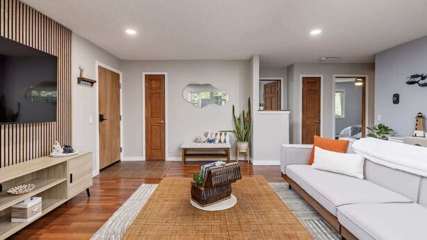 Una sala de estar moderna con un televisor de pantalla plana, un mueble de madera para entretenimiento, un sofá blanco y una mesa de centro.