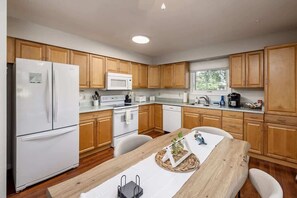 Une cuisine moderne avec des meubles en bois, des appareils électroménagers blancs et un coin repas doté d’une table en bois.