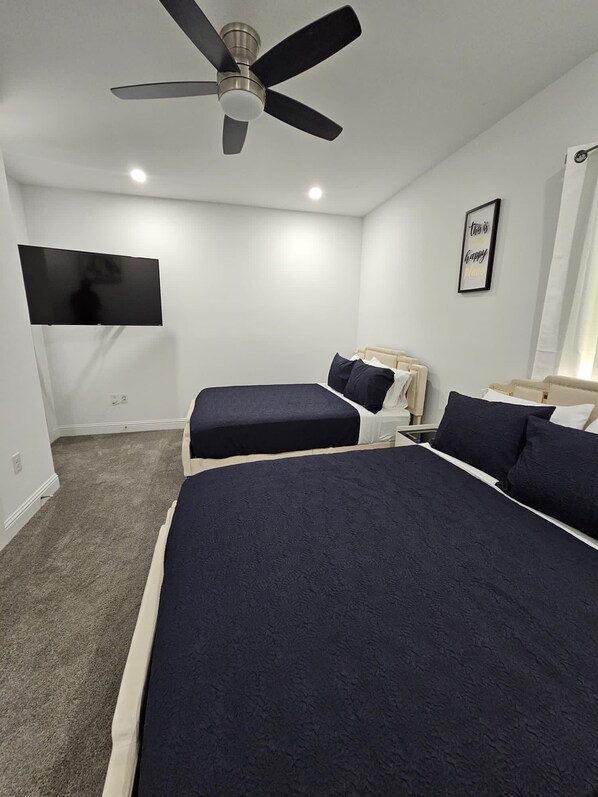 A bedroom with two beds, a ceiling fan, a flat-screen TV, and a motivational poster.