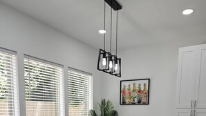 Un coin repas avec une table blanche, quatre chaises rembourrées, une plante en pot et un tableau encadré au mur.