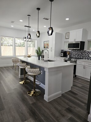 A modern kitchen with a large island, bar stools, and pendant lighting.