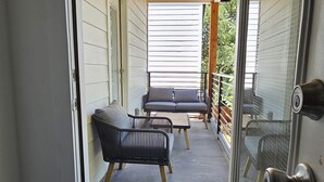 Une véranda couverte avec un ventilateur de plafond, un canapé gris et une chaise noire.