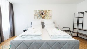Une chambre d’hôtel avec un lit, une table de chevet, une chaise, une échelle et un tableau au mur.