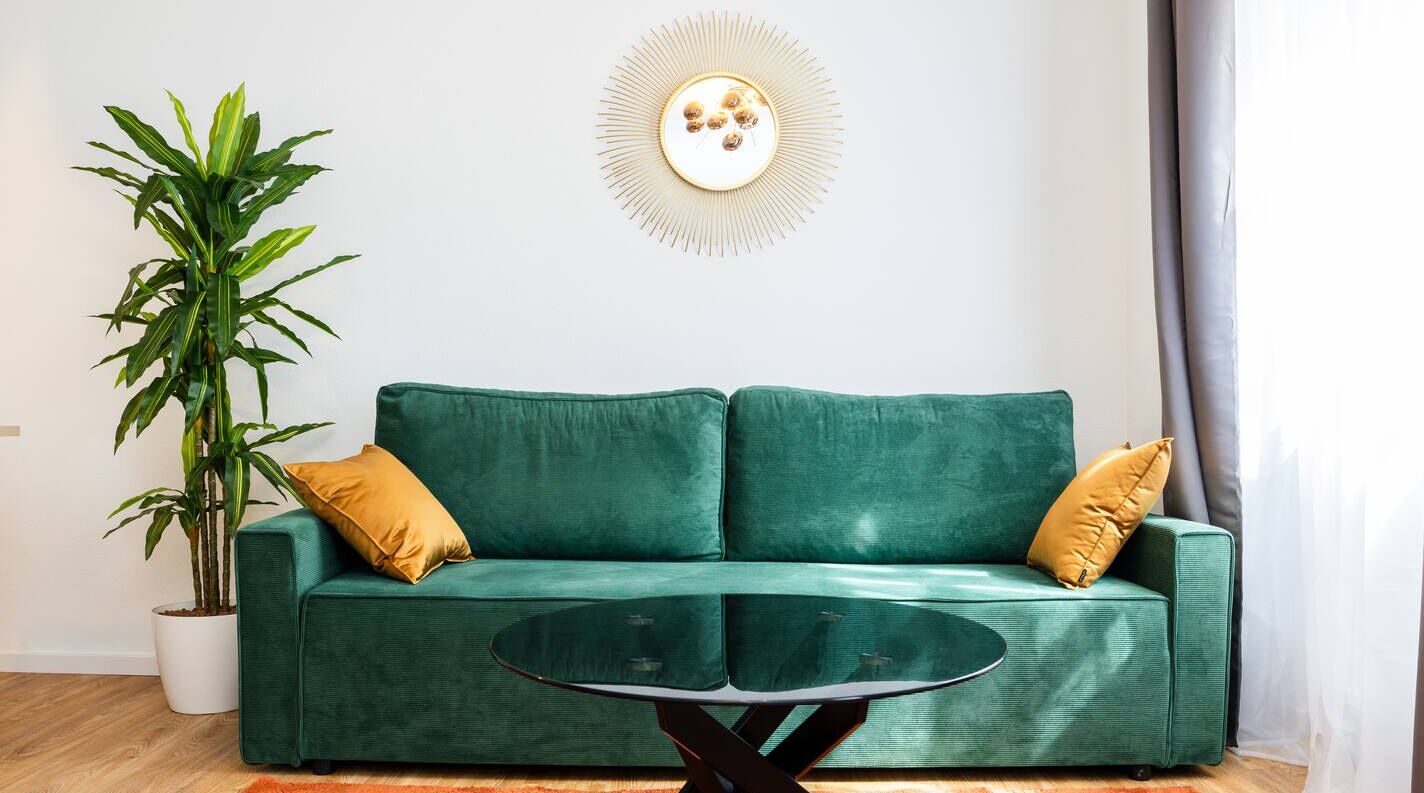 Ein grünes Sofa mit zwei gelben Kissen, einem Glastisch und einem Blumentopf.