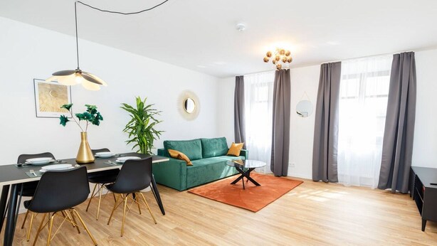 Un salon moderne comprenant un coin repas, un canapé vert, une table basse ronde et un téléviseur posé sur un meuble noir.