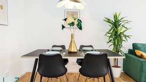 Un coin repas avec une table dressée pour quatre personnes, deux chaises noires aux pieds dorés, un vase doré contenant des feuilles vertes et un luminaire suspendu au plafond.