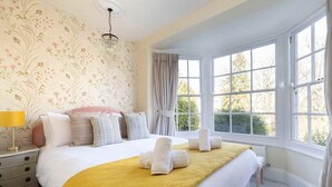 A neatly made bed with a yellow blanket, white pillows, and a floral wallpaper pattern. - Beautiful Two Bedroom Regency Apartment (Gloucestershire)