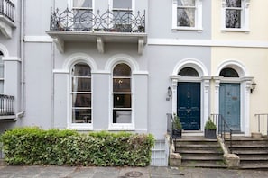 Una hilera de casas urbanas con fachadas blancas y grises, ventanas arqueadas y una puerta azul.