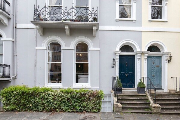 A row of townhouses with white and grey facades, arched windows, and a blue door.