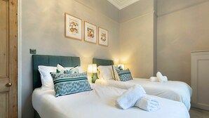 Ein Hotelzimmer mit zwei Betten, jeweils mit weißer Bettwäsche und grünen Kopfteilen. An der Wand über den Betten hängen drei gerahmte Bilder.