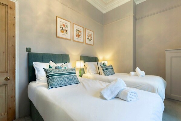 Une chambre d’hôtel avec deux lits, chacun agrémenté de draps blancs et d’une tête de lit verte. Trois tableaux encadrés sont accrochés au mur au-dessus des lits.
