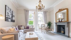 Ein Wohnzimmer mit einer Couch, einem Couchtisch und einem Kamin. Eine Chandelierleuchtre und ein großer Spiegel befinden sich über dem Kamin.