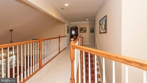 A hallway with a wooden staircase, white railings, and a carpeted floor.