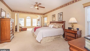 A bedroom with a large bed, a ceiling fan, a nightstand, and a dresser.