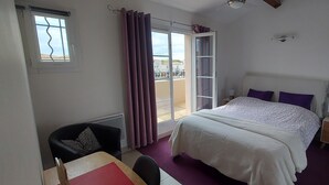Ein Schlafzimmer mit Bett, Stuhl, Nachttisch, Fenster mit Vorhängen und Blick nach draußen.