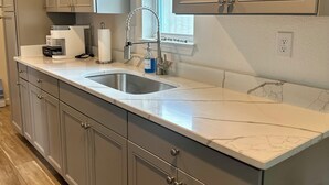 A kitchen with grey cabinets, a marble countertop, and a stainless steel sink.