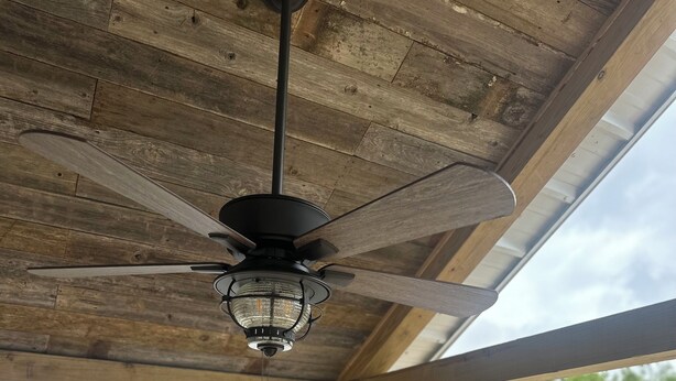 A wooden deck with a ceiling fan and a grill.