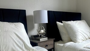 A hotel room with two beds, a nightstand with a lamp, and a wall-mounted artwork.