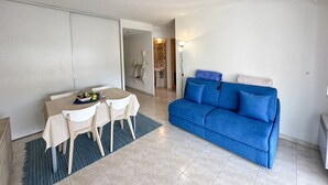 A living room with a blue sofa, a dining table with chairs, and a kitchen area in the background. - Charming Apartment in Cannes 10-min to beach (Cannes)
