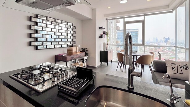 Una cocina moderna con estufa a gas, pileta de acero inoxidable y comedor con vista a la ciudad.
