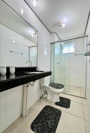 Um banheiro moderno com pia de bancada preta, azulejos brancos, box de vidro e vaso sanitário branco.