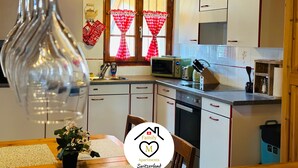 A kitchen with white cabinets, a microwave, a toaster, and a sink. There is a window with red curtains and a wooden ceiling. - Family M Apartments 15 - Center of Switzerland - Retro - Fire place (Kappel)