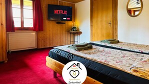A cozy bedroom with a wooden ceiling, a bed with floral bedding, a TV displaying 'Netflix', and a red carpet. - Family M Apartments 15 - Center of Switzerland - Retro - Fire place (Kappel)
