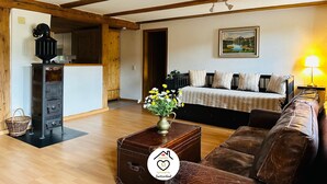 A cozy living room with a wooden ceiling, a bed with striped bedding, a brown leather sofa, and a small table with a vase of flowers. - Family M Apartments 15 - Center of Switzerland - Retro - Fire place (Kappel)