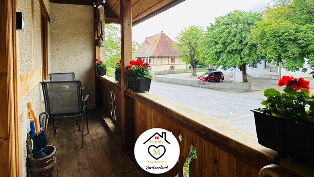 A wooden balcony with a clock, potted plants, and a view of a street with cars and trees. - Family M Apartments 15 - Center of Switzerland - Retro - Fire place (Kappel)