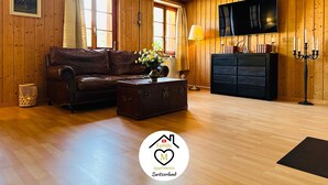 A cozy living room with a leather sofa, a coffee table with a vase of flowers, a TV mounted on the wall, and a wooden cabinet. - Family M Apartments 15 - Center of Switzerland - Retro - Fire place (Kappel)