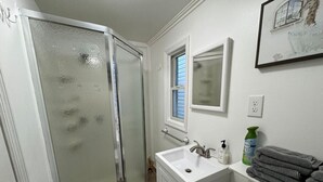 Un baño con mampara de vidrio, lavamanos con espejo y una pila de toallas.