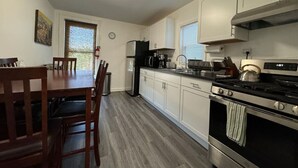 Una cocina con armarios blancos, una estufa, un refrigerador y una mesa de comedor con sillas.