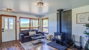 Ein gemütliches Wohnzimmer mit Kamin, Holzboden und großen Fenstern mit Blick ins Freie.