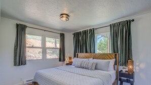 Ein Schlafzimmer mit einem großen Bett, zwei Nachttischen mit Lampen und Blick ins Freie durch die Fenster.