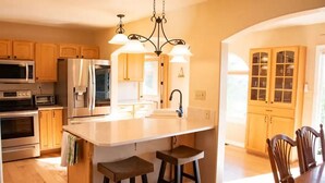 Een moderne keuken met houten kasten, een centraal eiland met krukken, roestvrijstalen apparatuur en een hanglamp.