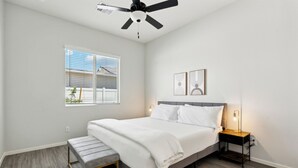 Ein Schlafzimmer mit Bett, Nachttisch, Bank, Deckenventilator, Fenster und Wandbild.